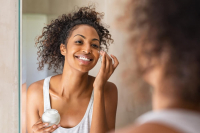 Imagem de uma moça se maquiando de frente para um espelho.