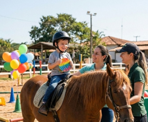 Criança em sessão de equoterapia acompanhada por duas monitoras